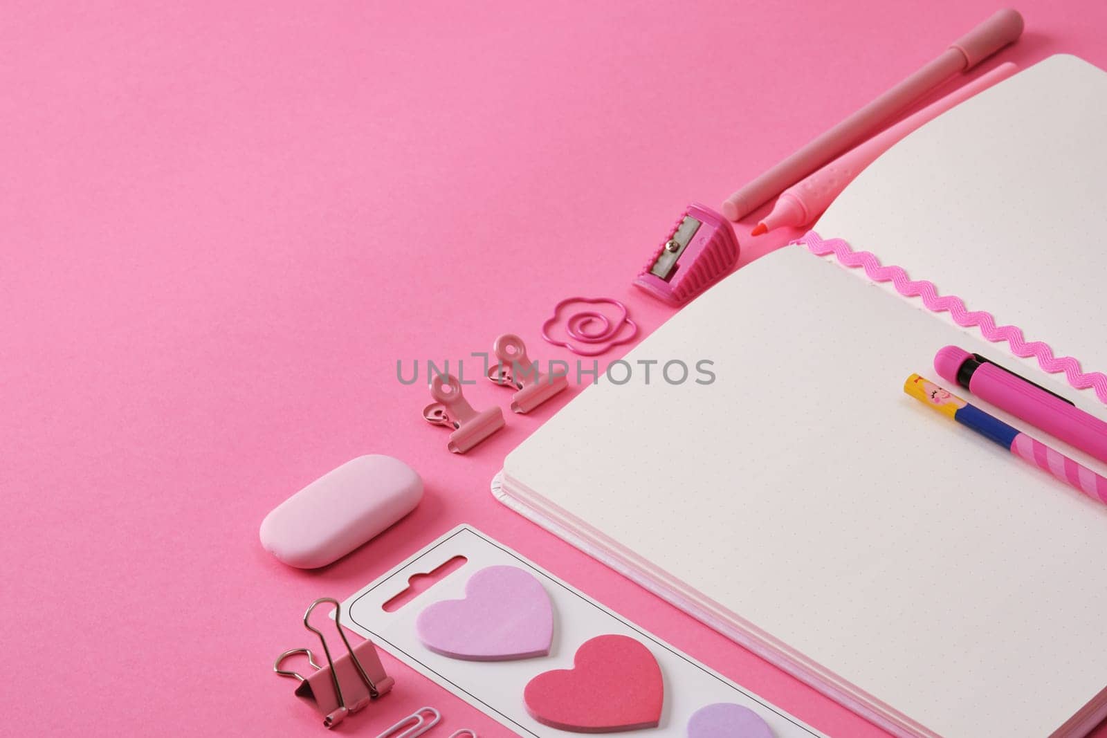 Stationery background in pink color, open notepad and office supplies. A place for your text.