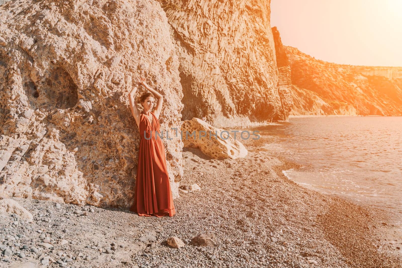 Woman red dress sea. Woman in a long red dress posing on a beach with rocks on sunny day. Girl on the nature on blue sky background