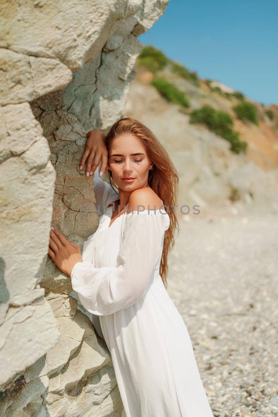 A woman in a white dress is standing on a rocky beach. Concept of serenity and tranquility, as the woman is enjoying the natural beauty of the beach