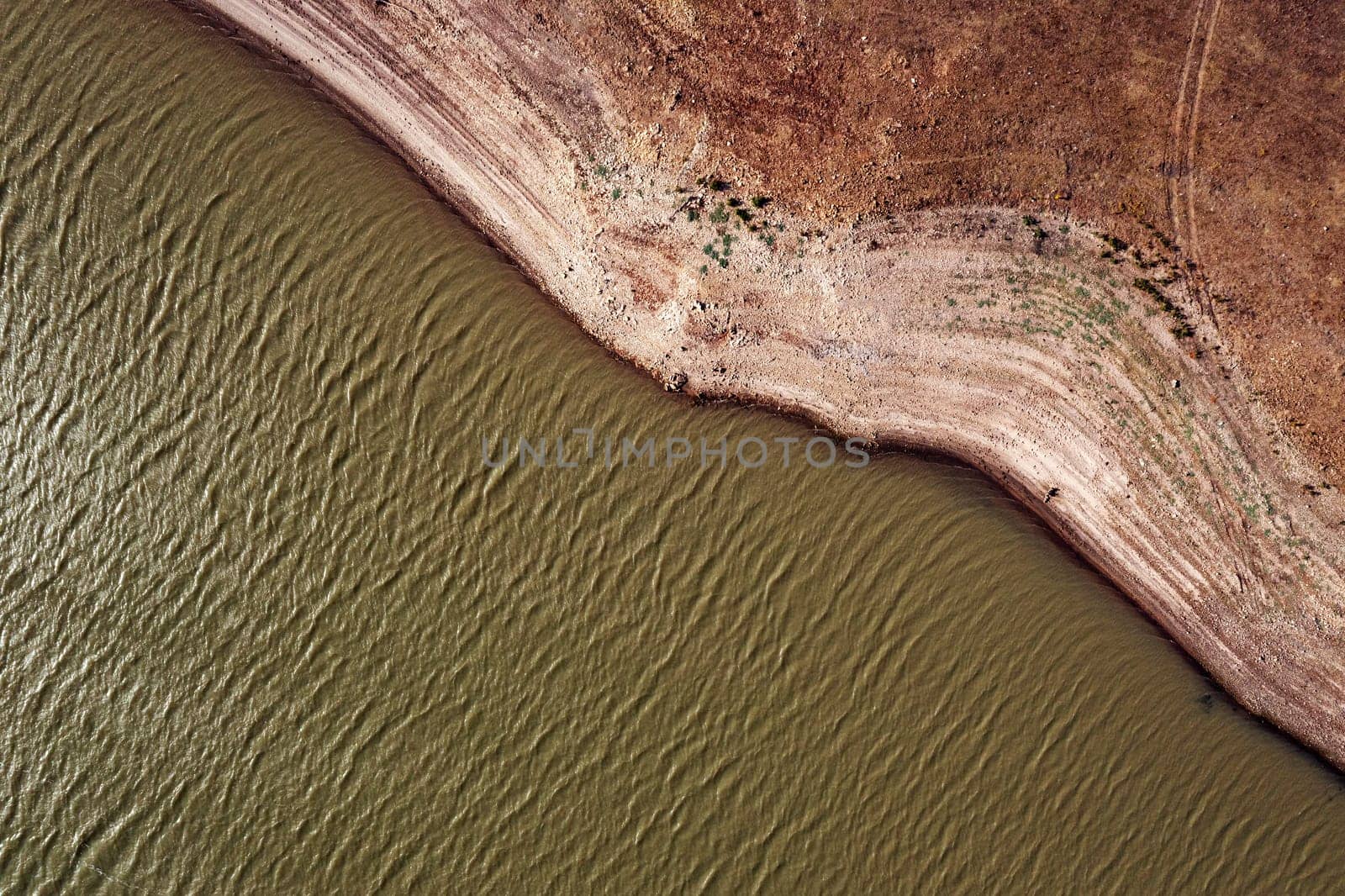 drone view of river with rippled water surface flowing near stony shore with dried surface in nature, concept of environment and ecology