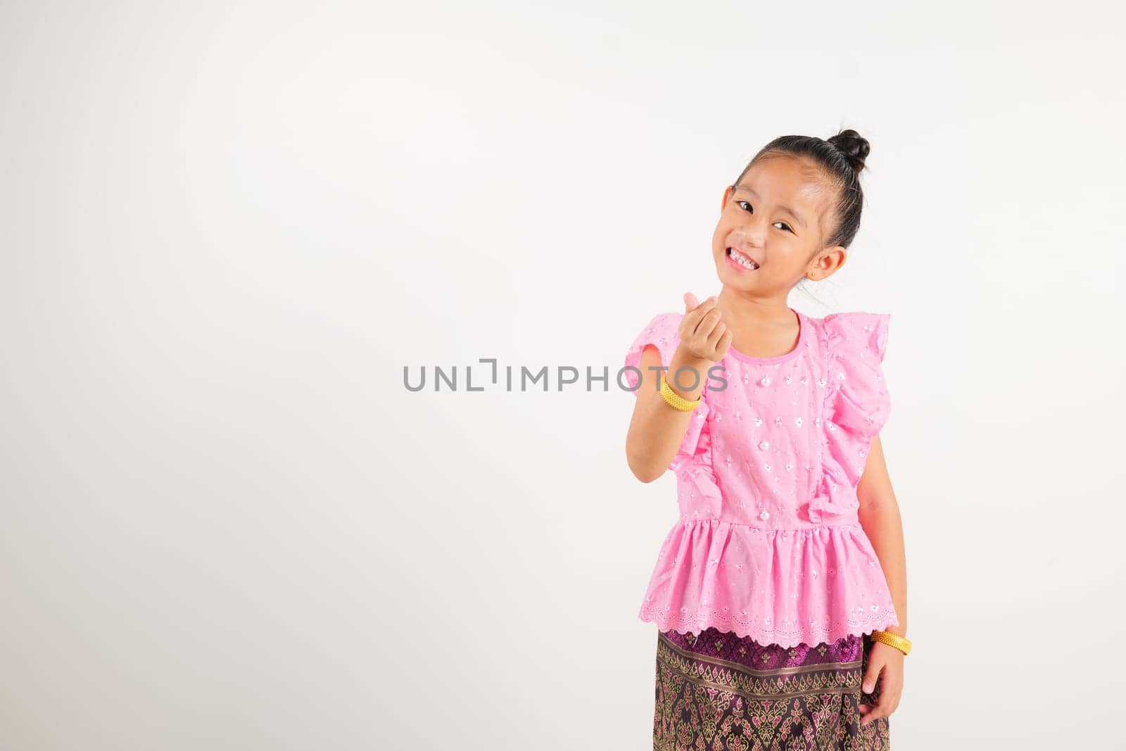 Portrait Thailand kid girl smiling traditional Thai dress costume showing mini heart sign with finger, studio isolated white background, kindergarten child expressing love and joy for Valentine Day