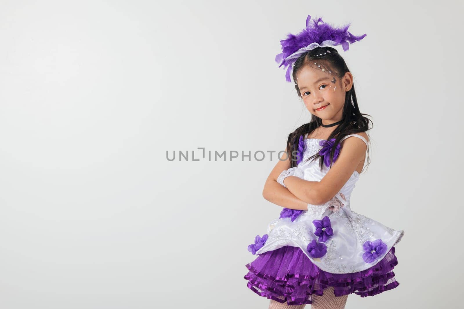 Cheerleader girl in a white and purple dress with a layered skirt, purple feather headpiece, and crossed arms. Studio photo with a clean white backdrop, showcasing her confident pose