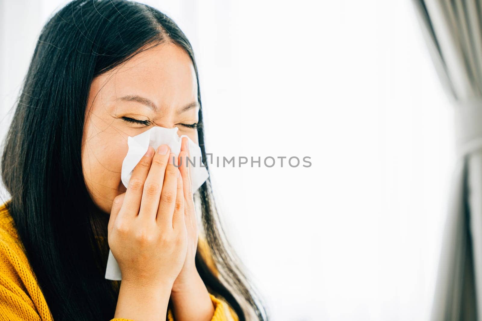 In an apartment a woman holds a tissue covering her nose due to coughing and sneezing. Portrait of a worried patient managing illness. Snot and handkerchief in hand.