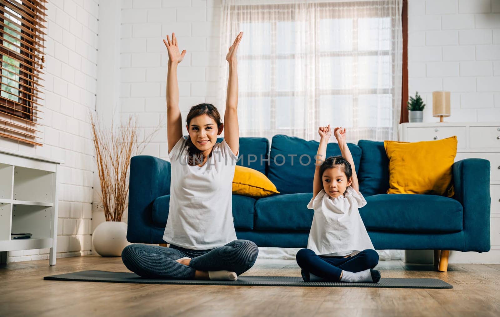 In their cozy home a mother and her delightful daughter practice family yoga embracing smiles as they stretch and balance together fostering togetherness and happiness.
