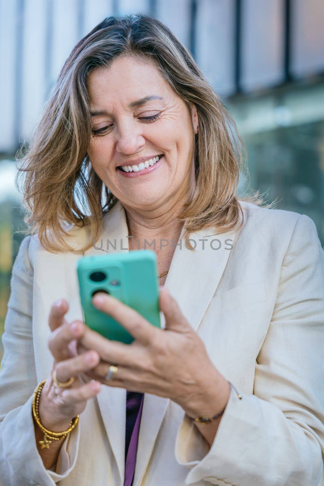 Smiling middle-aged businesswoman using a smartphone outdoors in a modern urban setting.