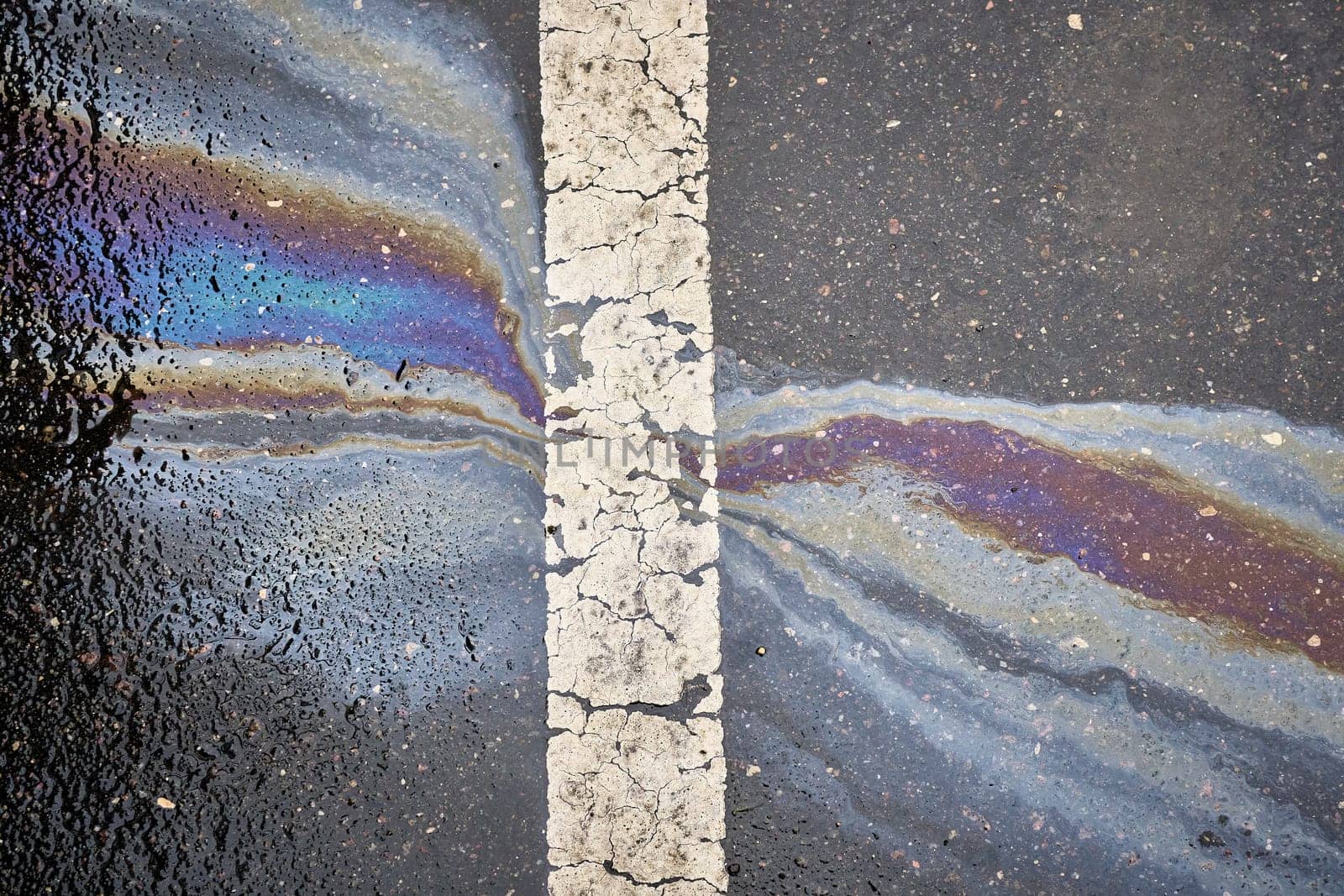 Gasoline or oil polluting wet asphalt road creating rainbow pattern next to a white dividing line.