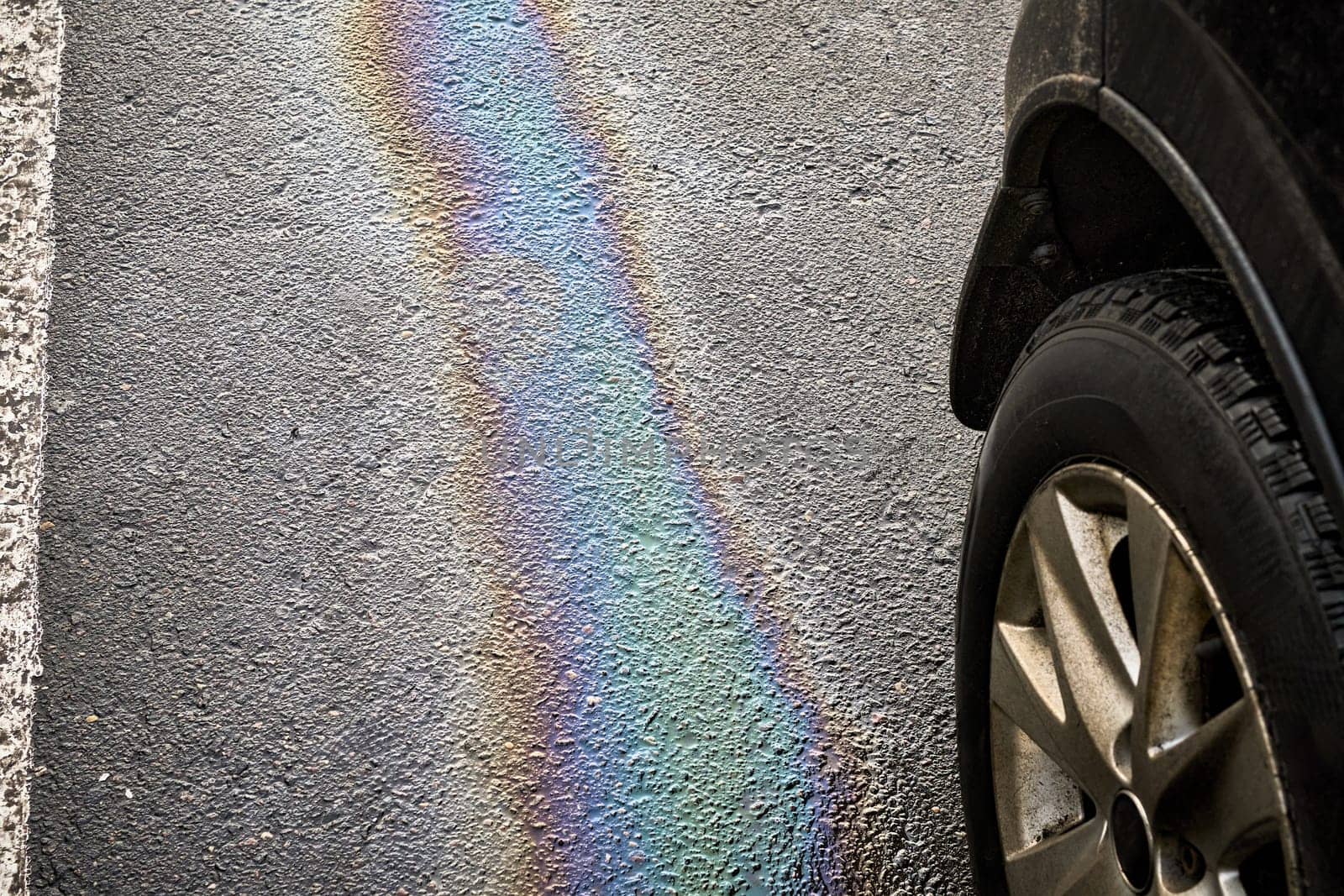 Gasoline or oil spill creating rainbow sheen on asphalt parking lot next to car tire