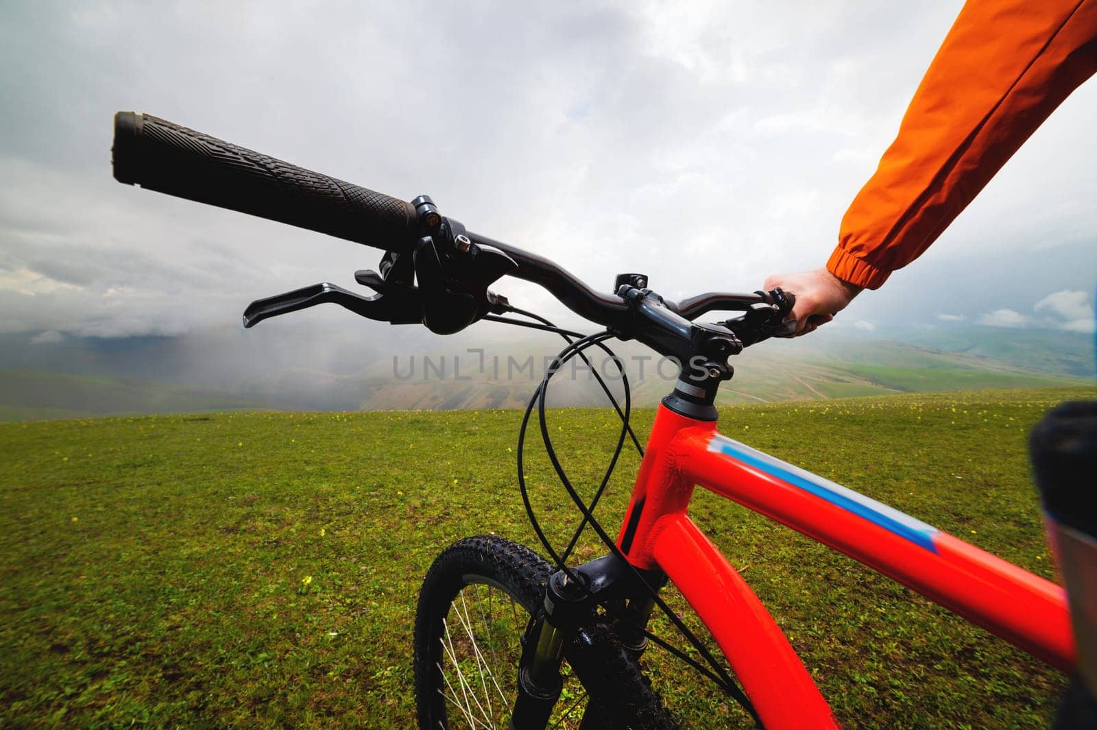 First person view of the handlebars and frame of a bicycle, in the background there are mountains in a fog of clouds. mountain bike on a green meadow on a hill by yanik88