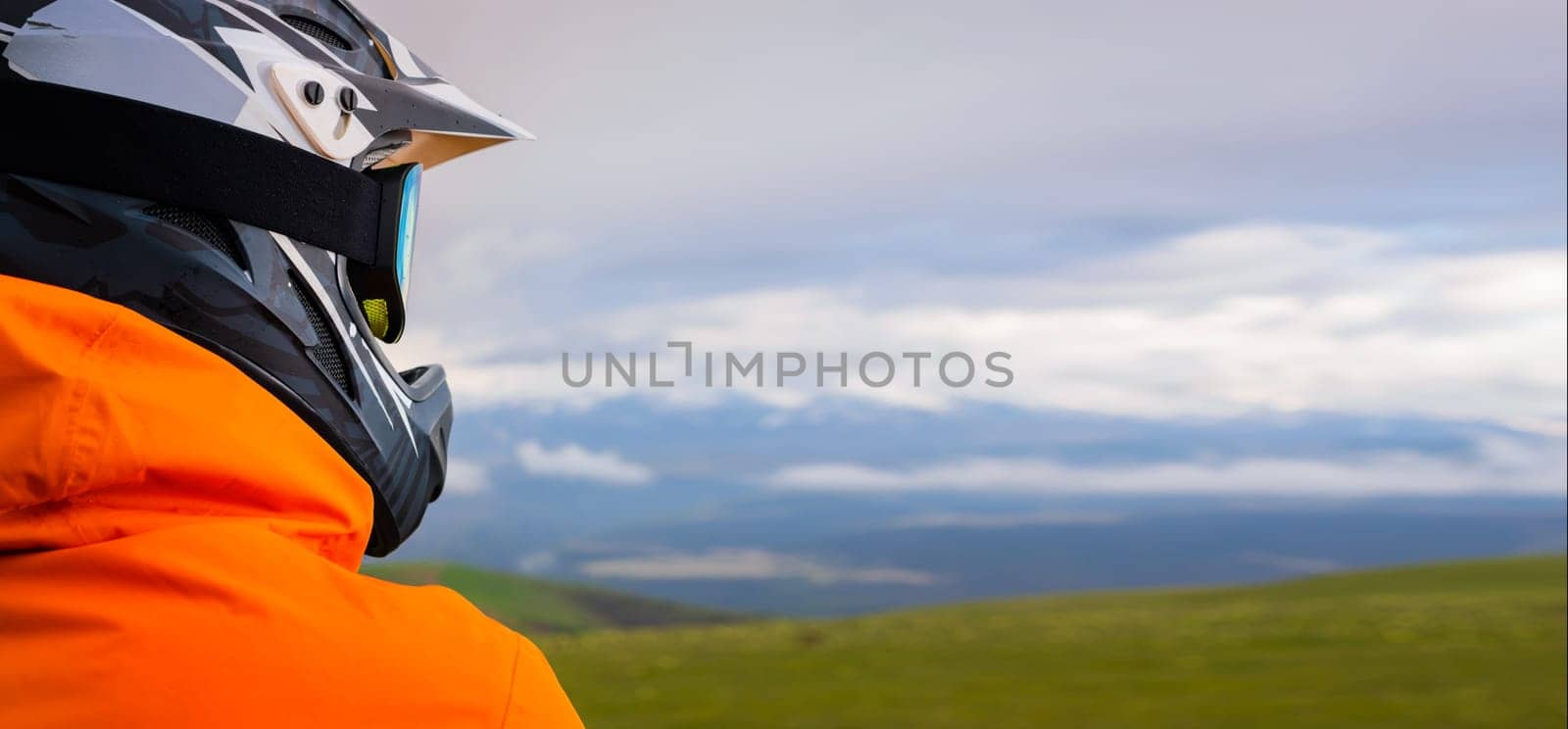 portrait of a cyclist or motorcyclist on top of a mountain, viewed from the back, looking at the mountain range in the clouds. panoramic mountain view, sport and banner concept for advertising by yanik88