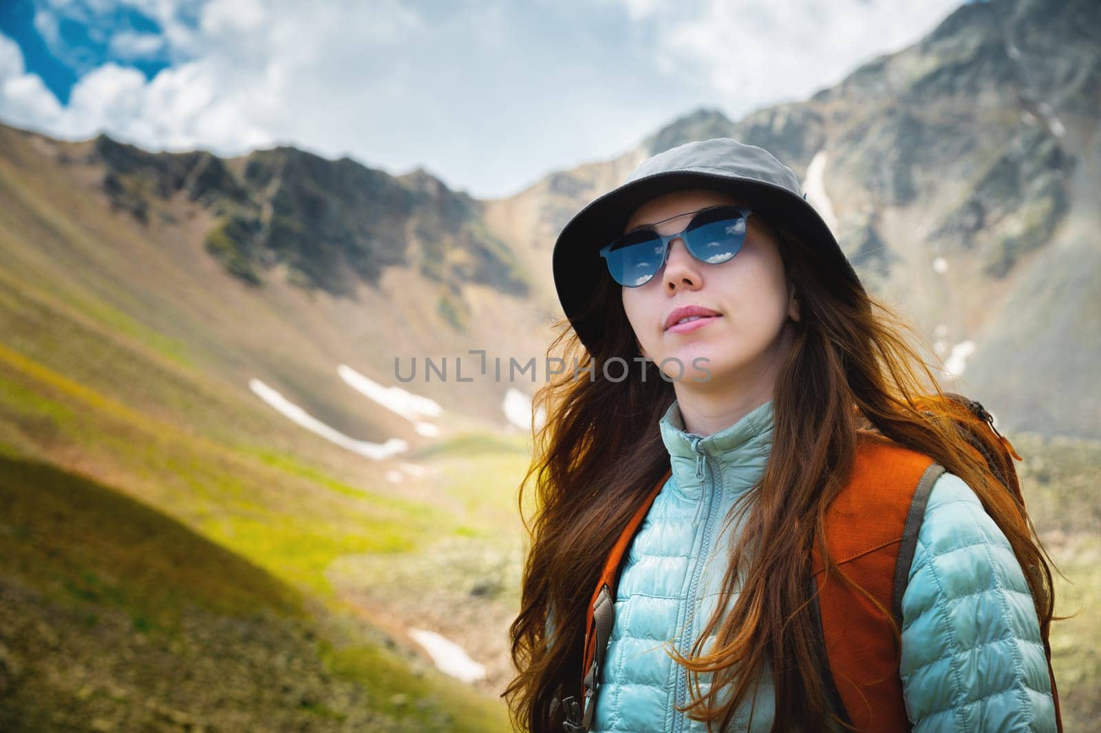 stylish female traveler in fashionable sunglasses and with backpack smiling on top of mountains in summer sunny season, travel concept.