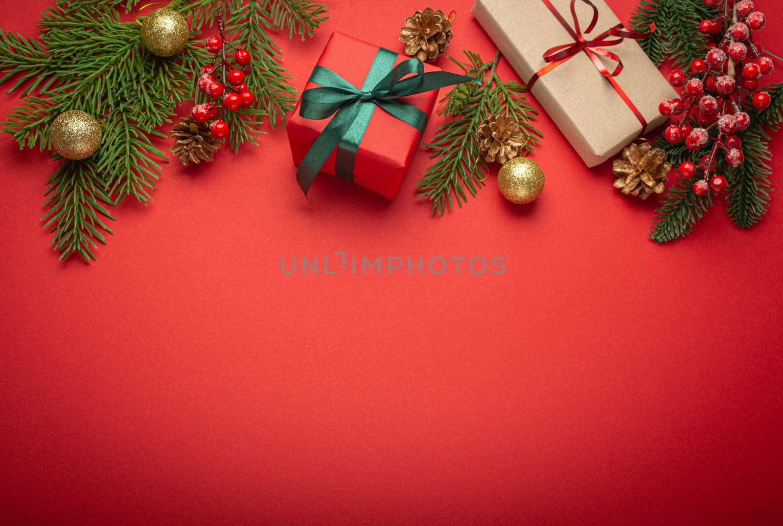 Christmas or New Year celebration red paper festive background with decoration fir tree, wrapped present boxes, cones, berries, sparkly red balls. Space for text. by its_al_dente