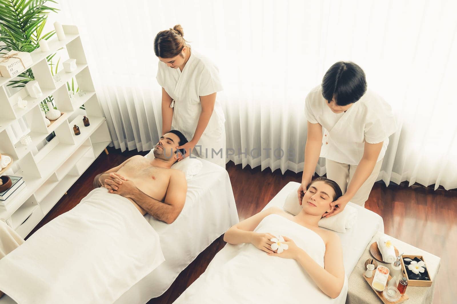 Caucasian couple enjoying relaxing anti-stress head massage and pampering facial beauty skin recreation leisure in dayspa modern light ambient at luxury resort or hotel spa salon. Quiescent