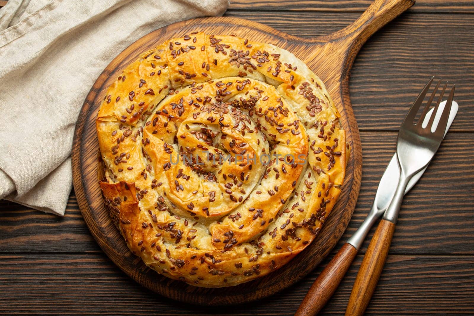 Burek made of phyllo dough with filling on cutting board, dark brown wooden rustic background top view. Traditional savoury spiral pie of Balkans, Middle East and Central Asia by its_al_dente