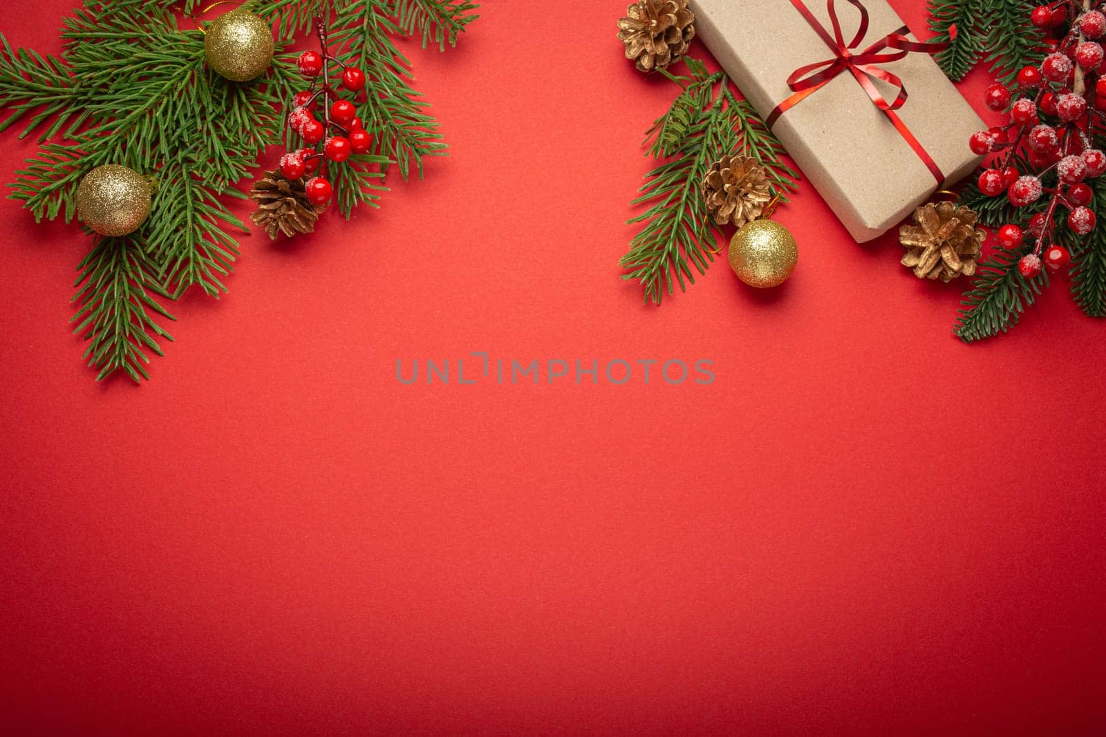 Christmas or New Year celebration red paper festive background with decoration fir tree, wrapped present boxes, cones, berries, sparkly red balls. Space for text..