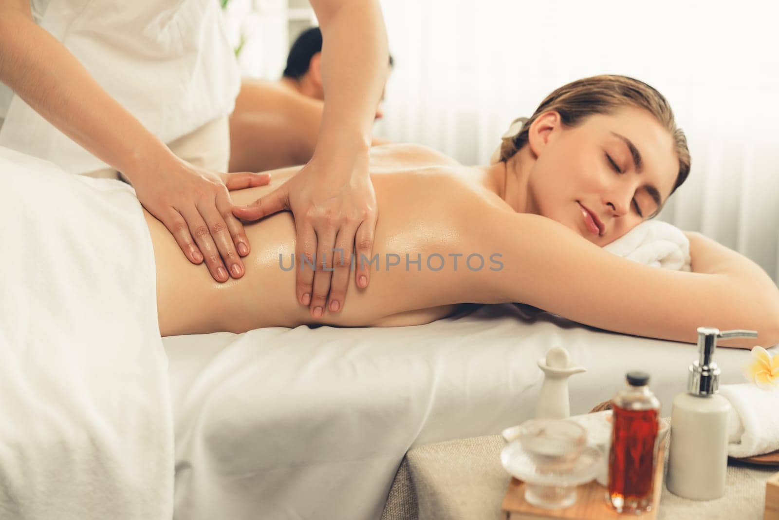 Caucasian couple customer enjoying relaxing anti-stress spa massage and pampering with beauty skin recreation leisure in day light ambient salon spa at luxury resort or hotel. Quiescent
