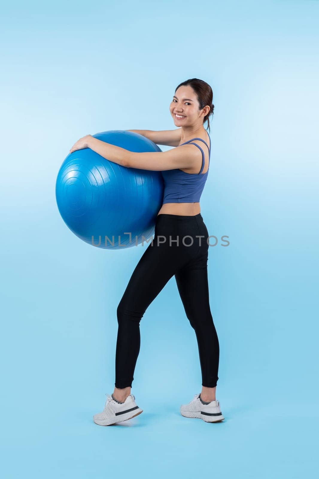 Young attractive asian woman portrait in sportswear with fit ball targeting on abs muscle for effective energetic daily workout routine. Studio shot and isolated background. Vigorous