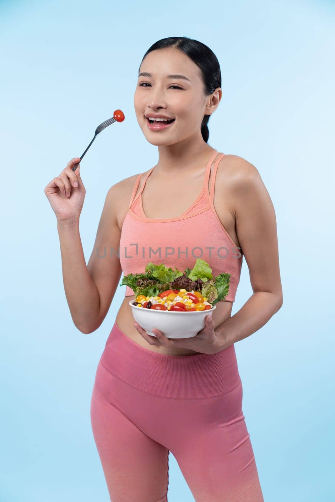 Young sporty Asian woman in sportswear holding salad bowl fill with vibrant of fruit and vegetable. Natural youthful and fit body lifestyle with balance nutrition on isolated background. Vigorous