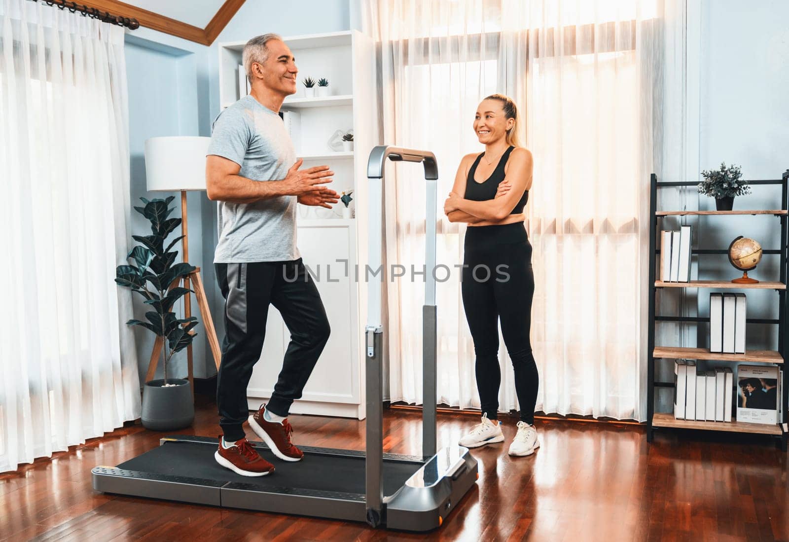 Active senior couple running on tread running machine at home together in full body shot as fitness healthy lifestyle and body care after retirement for pensioner. Clout