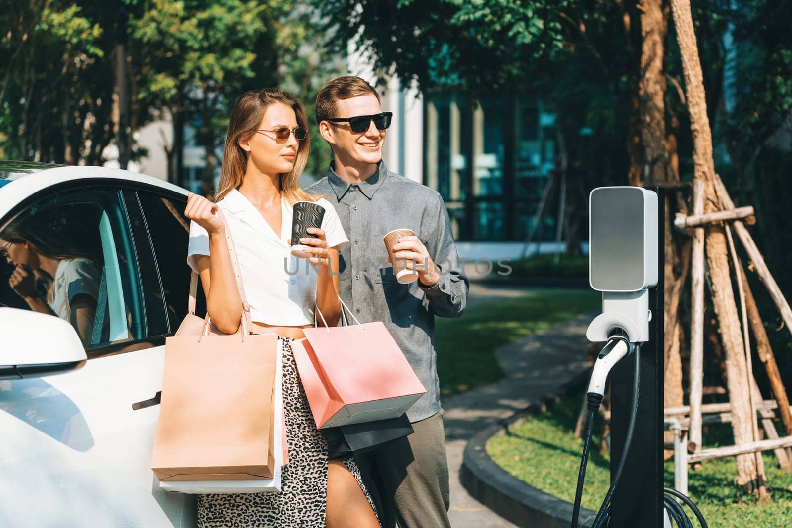 Young couple travel with EV electric car in green sustainable city innards by biancoblue