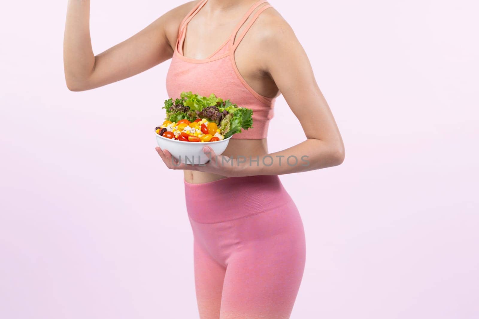 Young sporty Asian woman in sportswear holding salad bowl fill with vibrant of fruit and vegetable. Natural youthful and fit body lifestyle with balance nutrition on isolated background. Vigorous