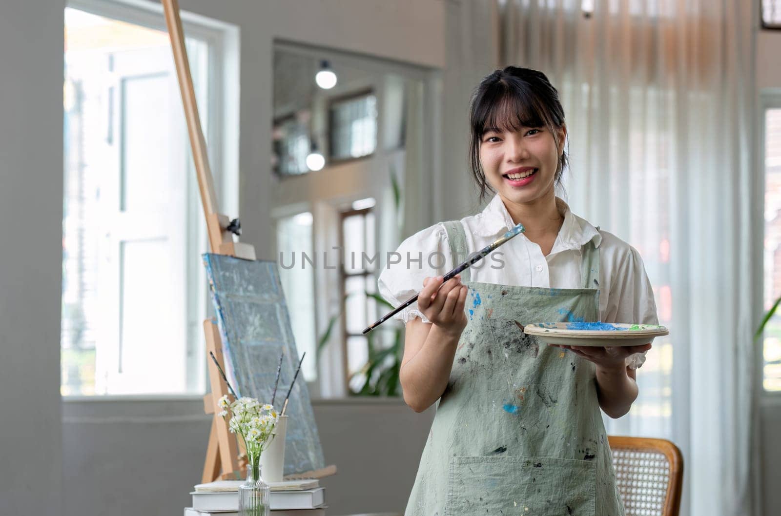 Portrait of a young female artist working on an abstract acrylic canvas painting in an art painting studio. by wichayada