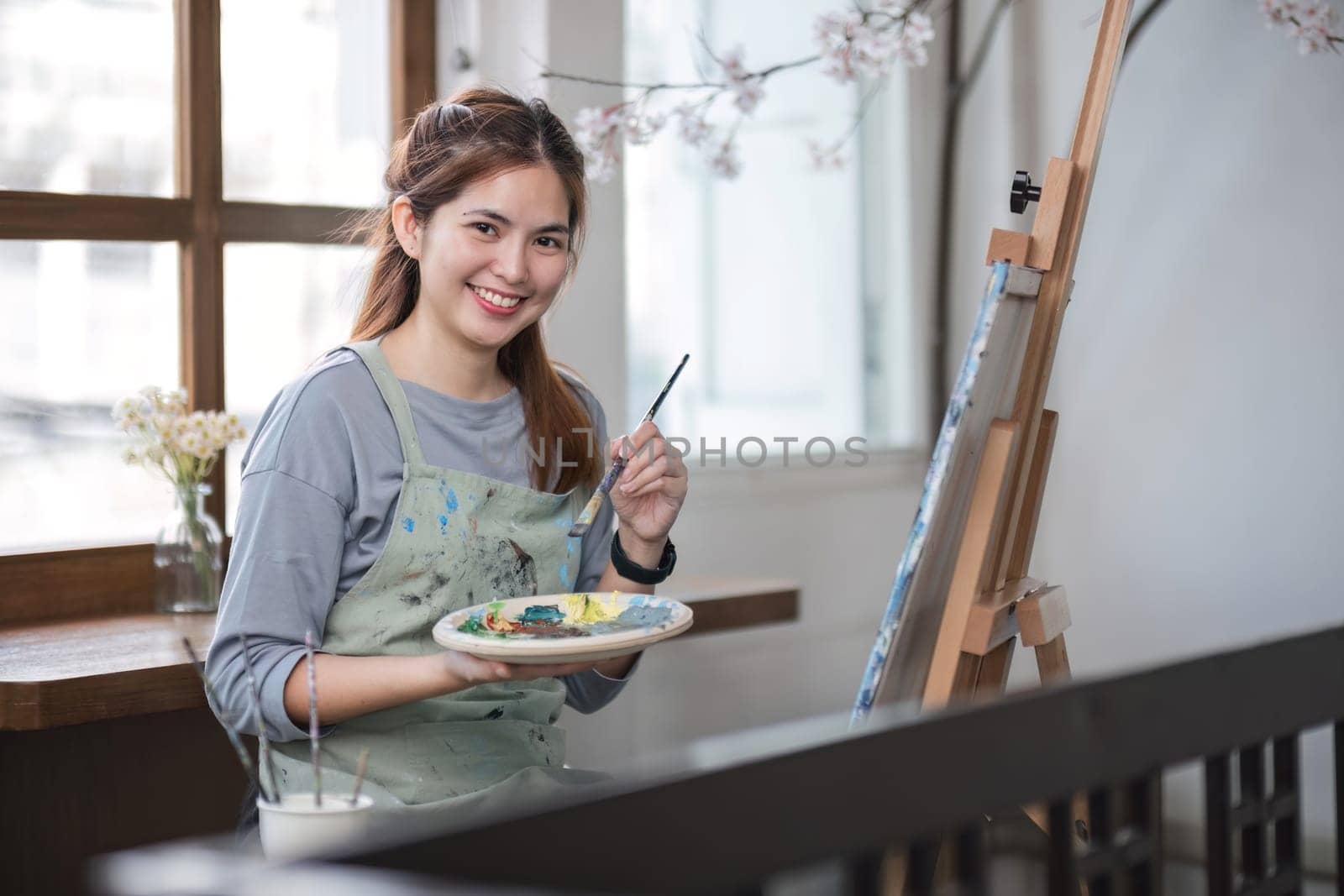 Portrait of a young female artist working on an abstract acrylic canvas painting in an art painting studio. by wichayada