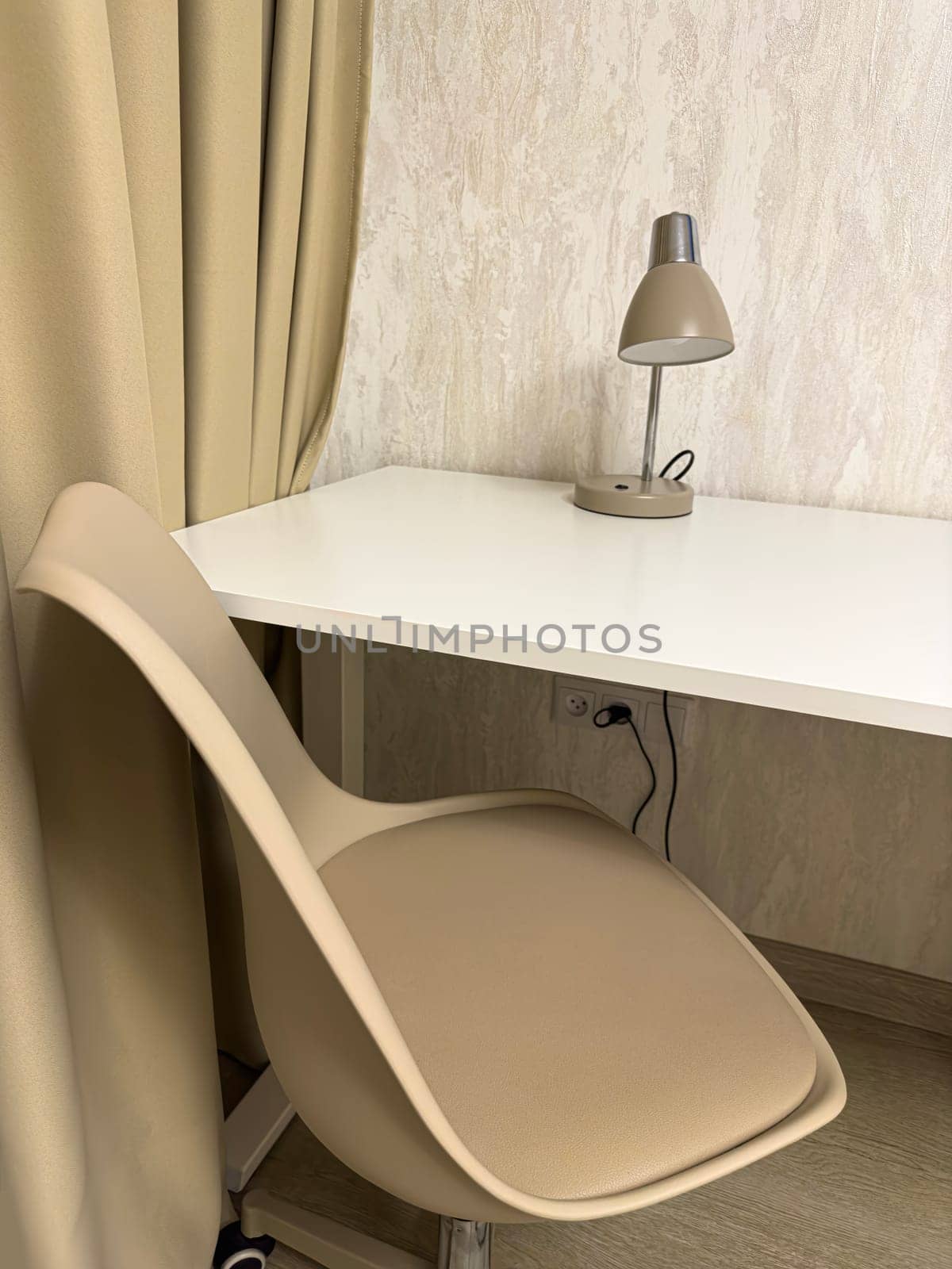 A minimalist workspace featuring a stylish beige chair and a modern lamp on a sleek white desk, surrounded by soft curtains, creating a calm and inviting atmosphere.