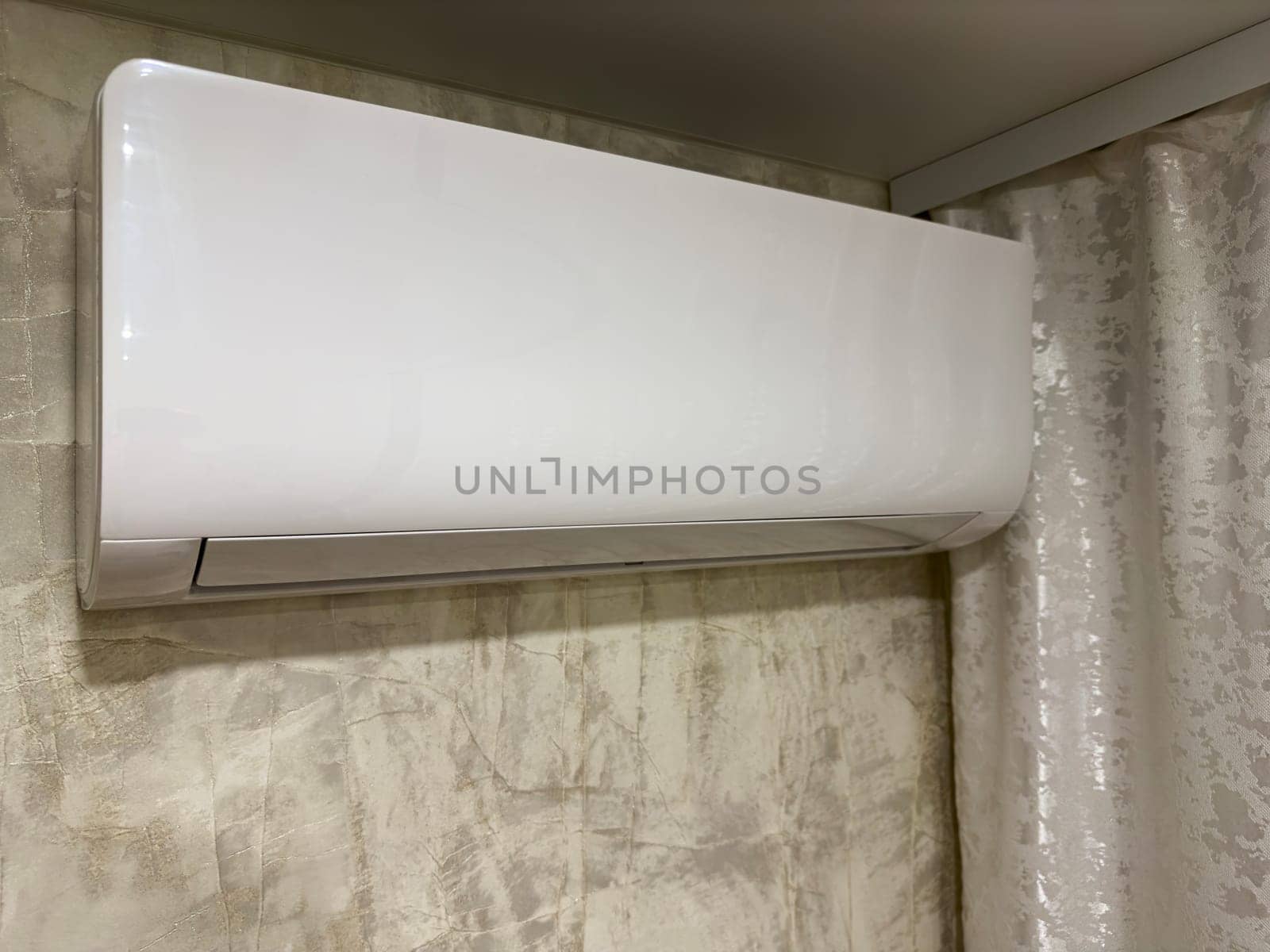 A sleek, white wall-mounted air conditioning unit is installed in a contemporary room with textured walls and soft lighting, highlighting its efficient design for climate control.