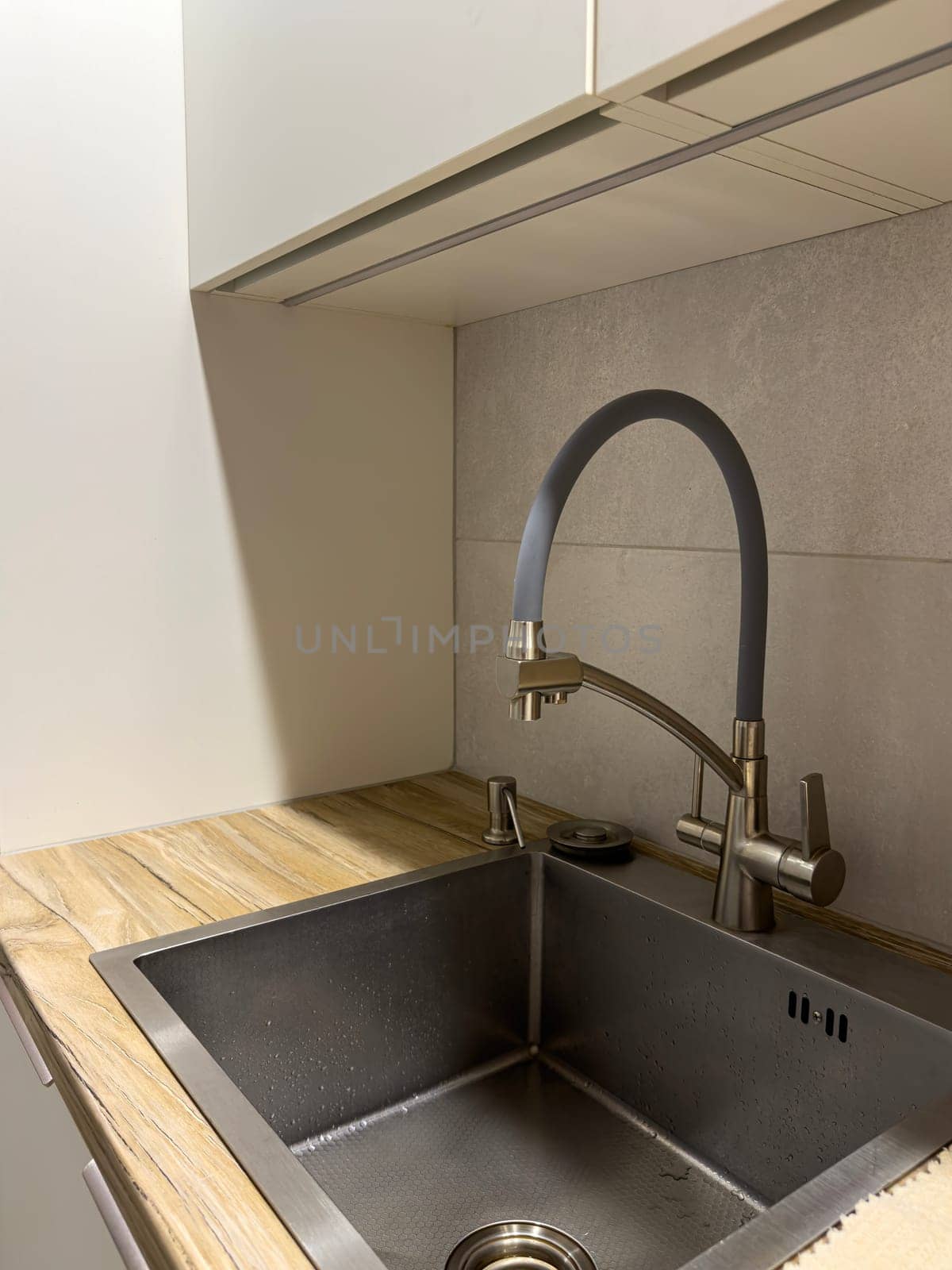 An elegant kitchen setup featuring a sleek stainless steel sink with a modern faucet. The wooden countertop adds warmth to the minimalistic design, perfect for contemporary homes.