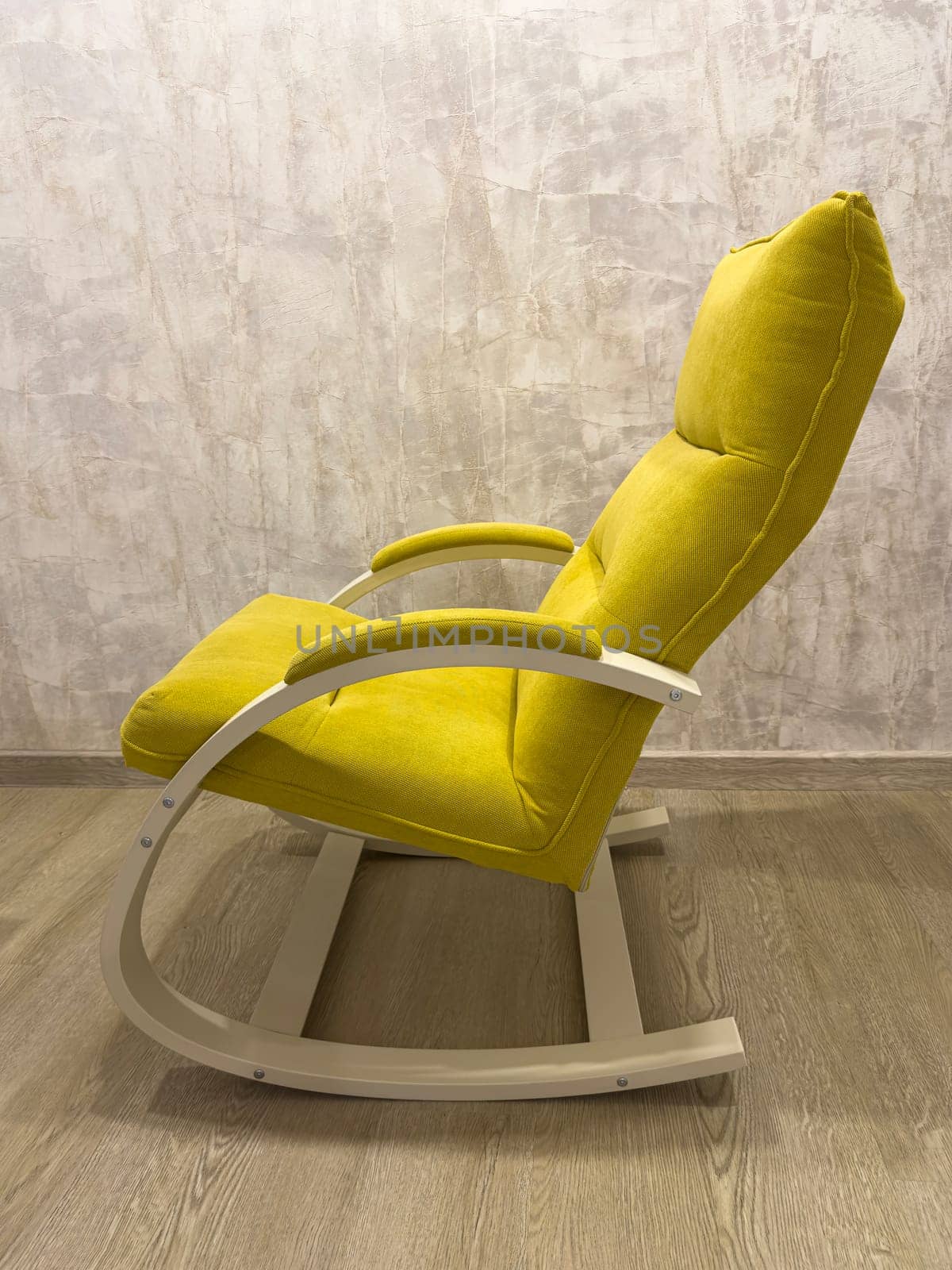 A vibrant yellow rocking chair is positioned on a light wooden floor against a textured wall. This chair features a simple, ergonomic design ideal for relaxation in modern interiors.