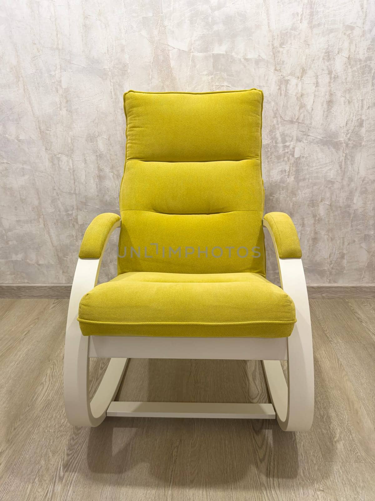 A bright yellow rocking chair features textured upholstery and a sleek white frame in a contemporary room. The chair is centered in a minimalist space with neutral tones.
