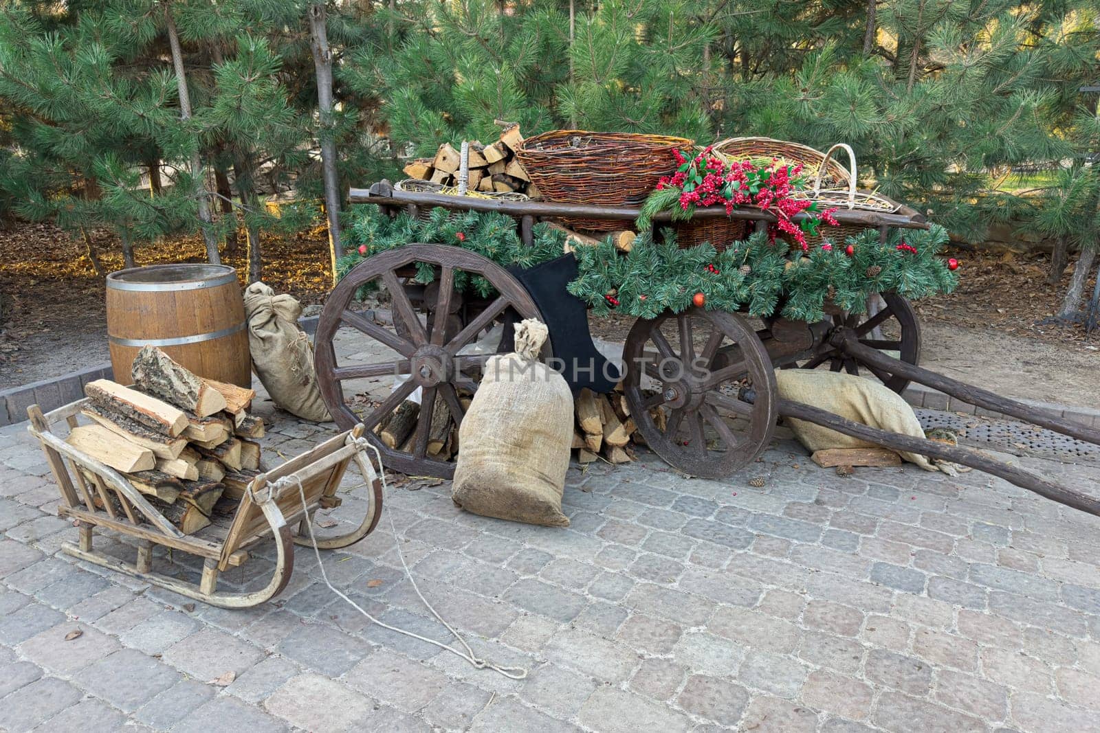 A rustic wooden cart filled with firewood and decorative flowers rests in a tranquil outdoor location. Bags of wood sit nearby, enhancing the charming atmosphere.