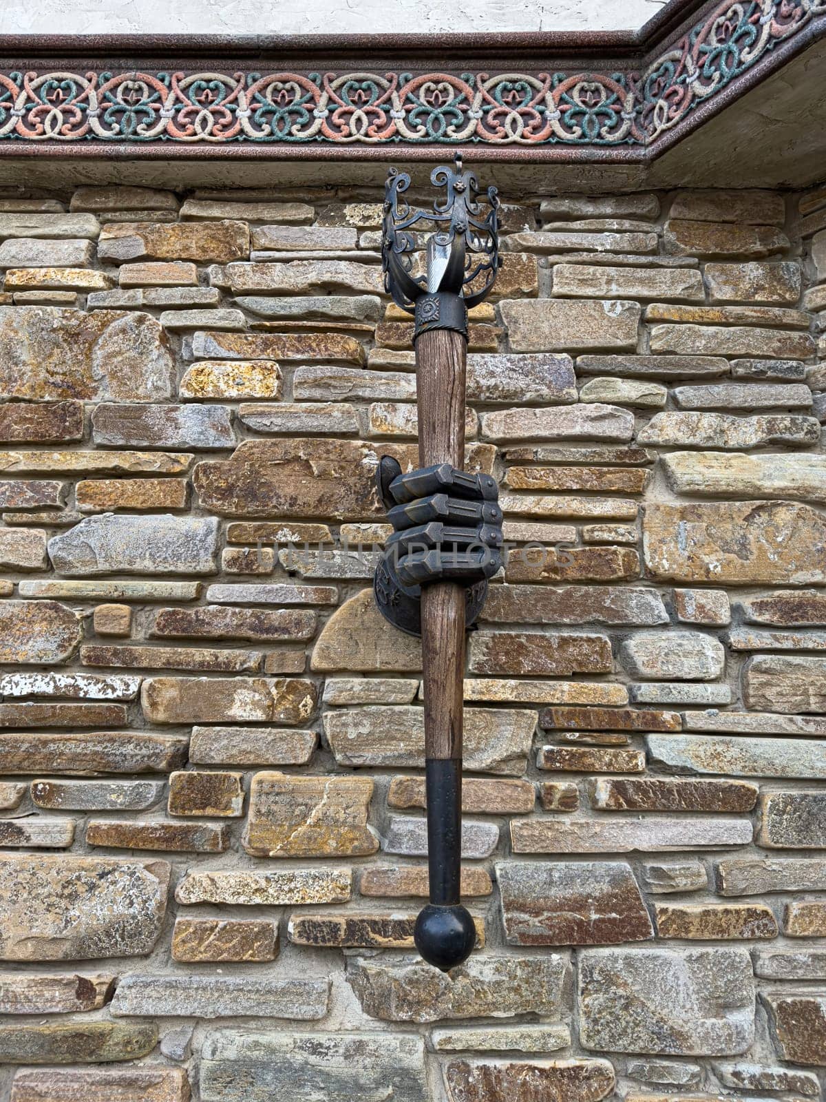 A creative wall sculpture displays a hand gripping a decorative staff, mounted on a rustic stone wall. The art piece adds character and intrigue to the setting, highlighting craftsmanship.