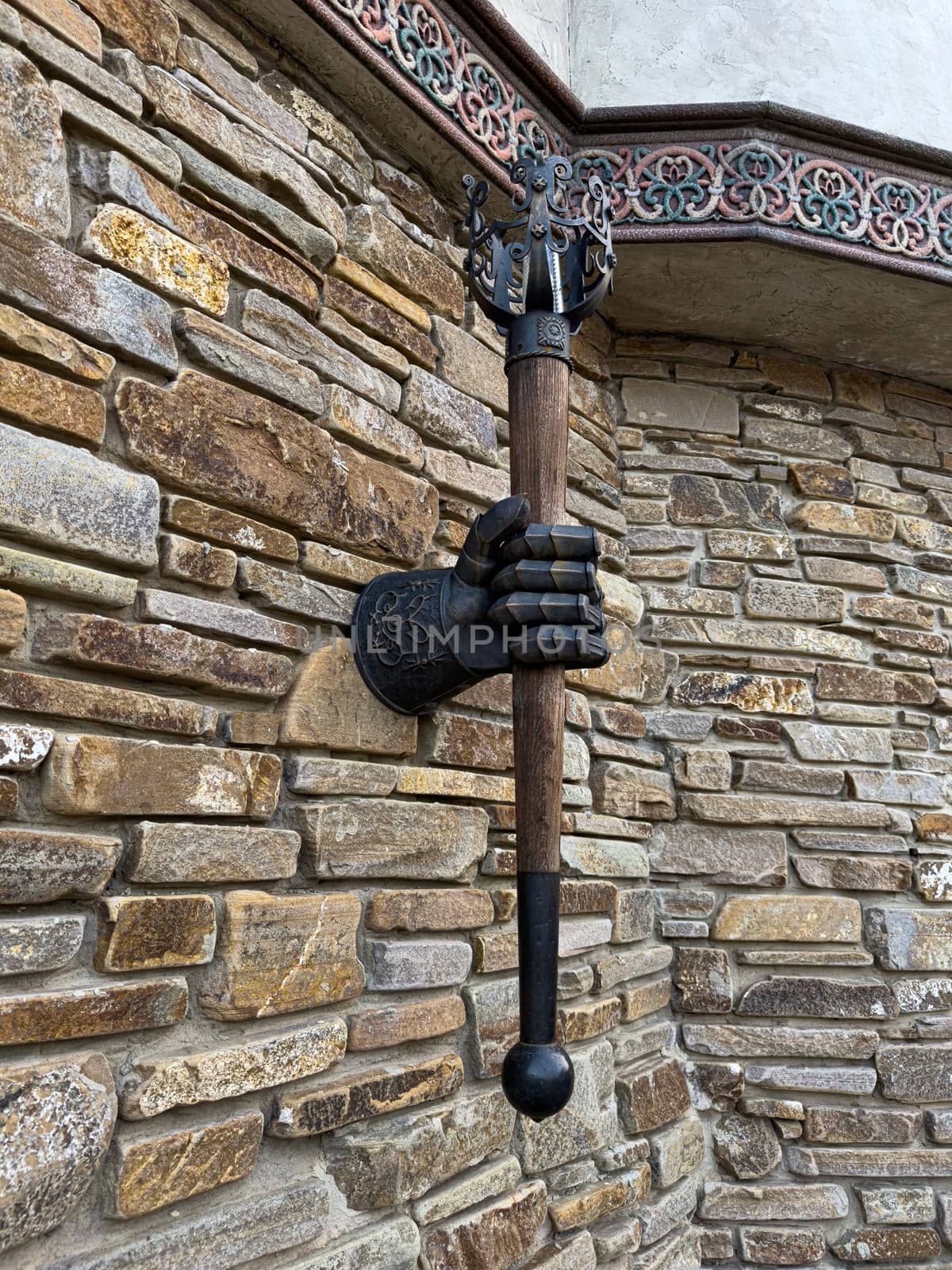 A striking wall fixture consists of a realistic hand grasping a mace, mounted on a textured stone wall. This artistic piece adds a medieval touch to the exterior design.