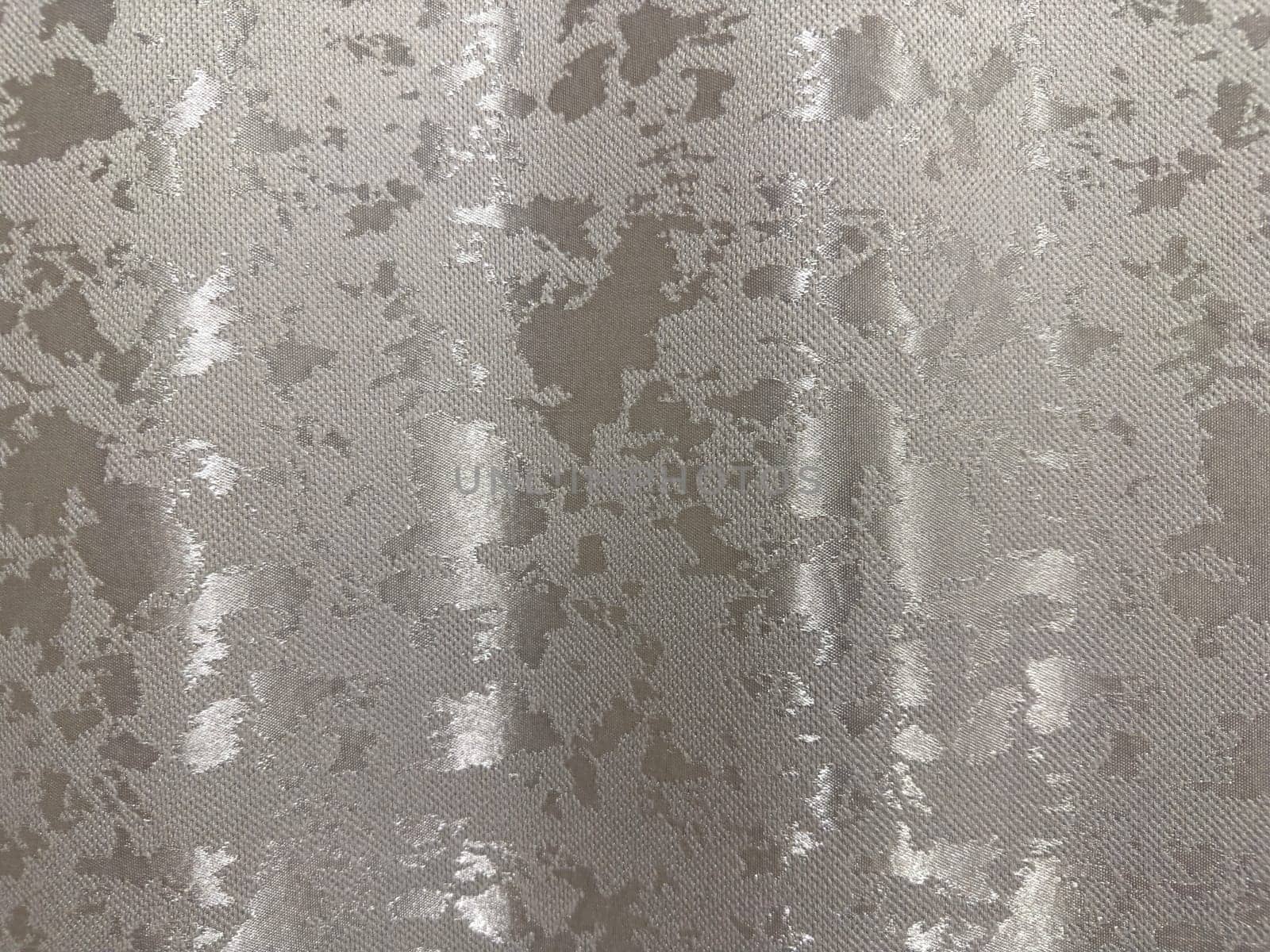Shimmering silver fabric features a detailed textured pattern, ideal for fashion, upholstery, or decorative projects. The surface reflects light, adding depth and sophistication to any design.