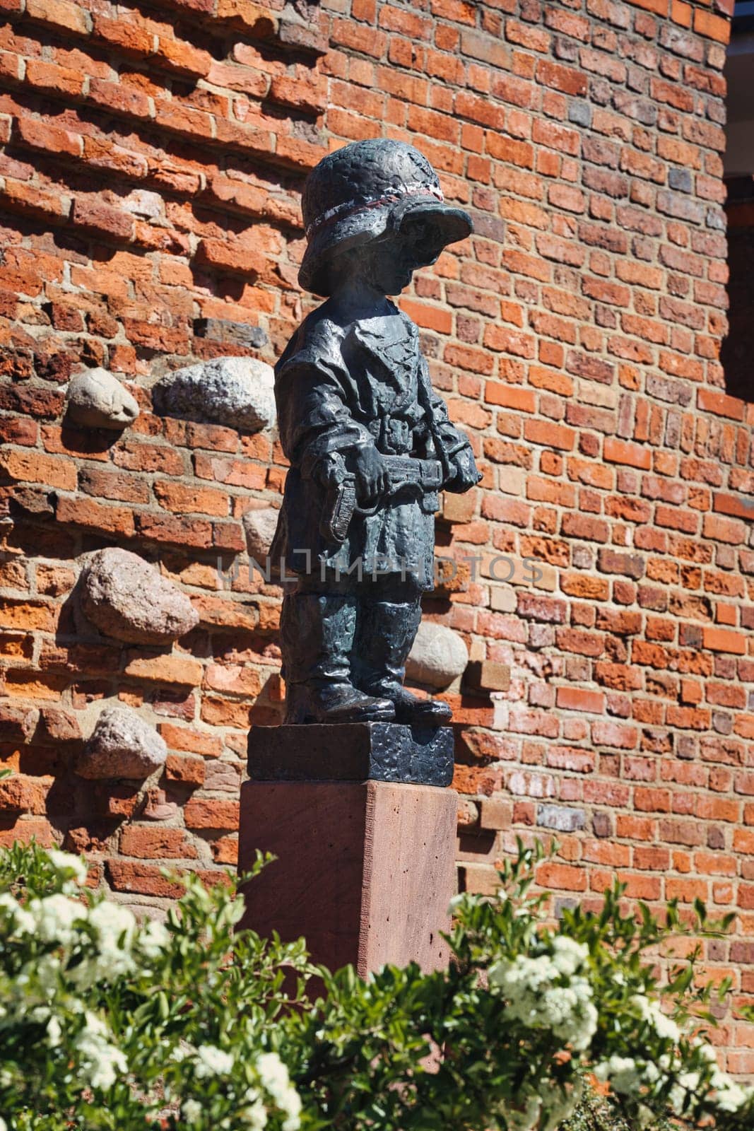 A poignant image of the Little Insurgent Monument in Warsaw, Poland. This bronze statue commemorates the children who fought in the Warsaw Uprising of 1944. The red-brick wall and greenery in the background add depth to this touching tribute.