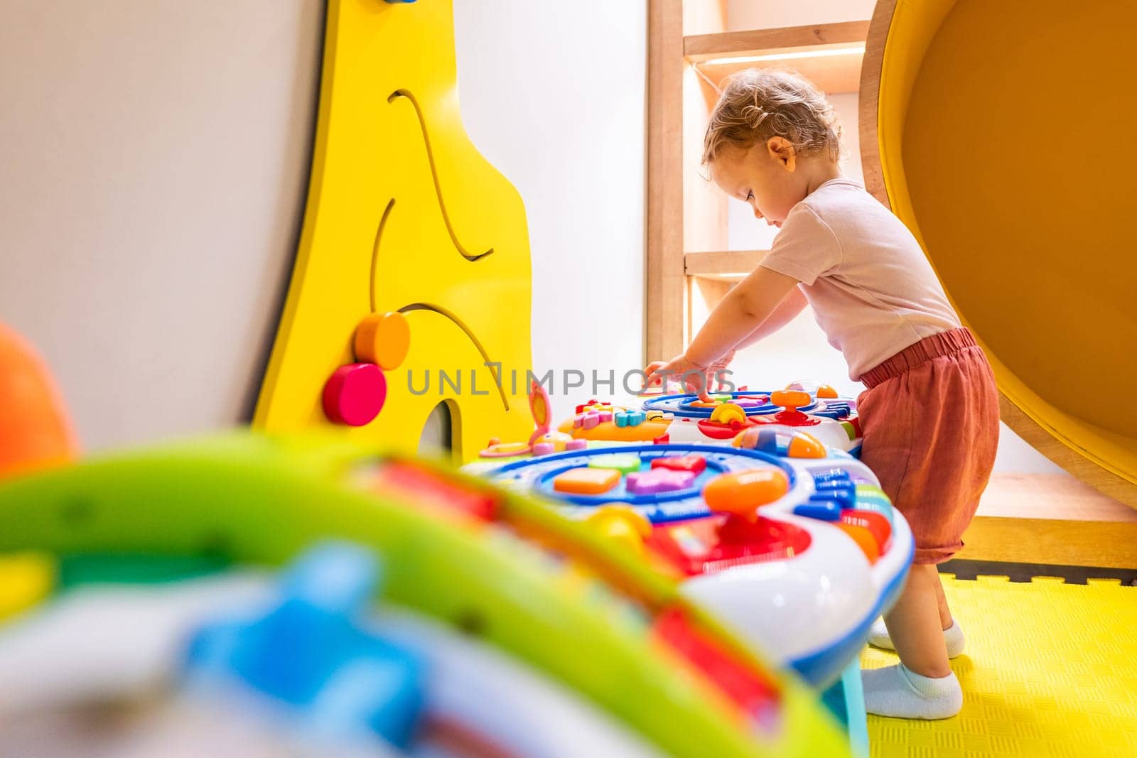 Toddler playing with interactive toy table featuring lights, sounds, and shapes in a play area