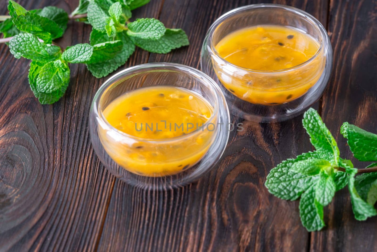 Two glass bowls filled with passion fruit pulp and fresh mint on a dark rustic wooden background