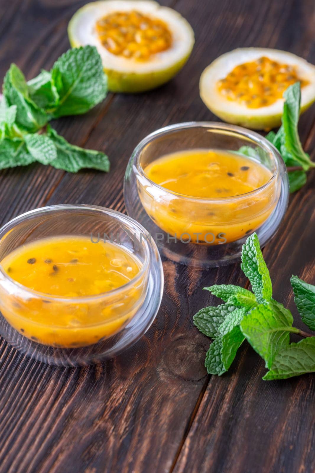 Two glass bowls filled with passion fruit pulp and fresh mint on a dark rustic wooden background
