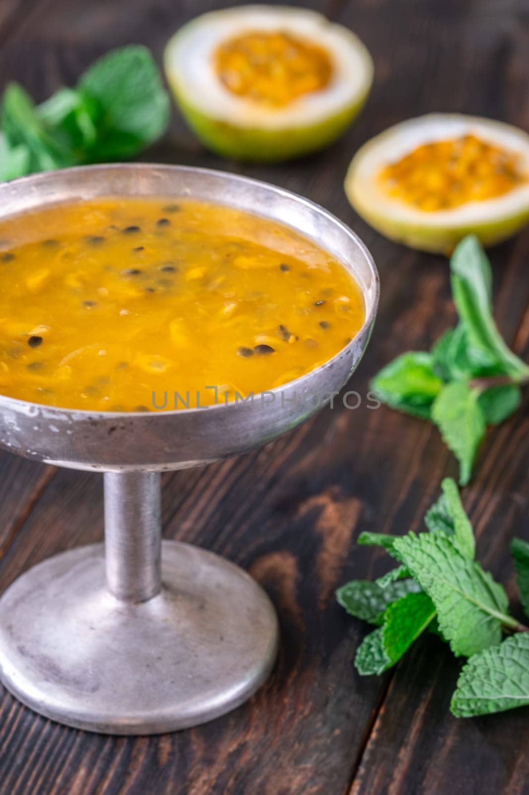 Passion fruit pulp, halved fruit, and fresh mint in a rustic metal vase on a dark wooden background