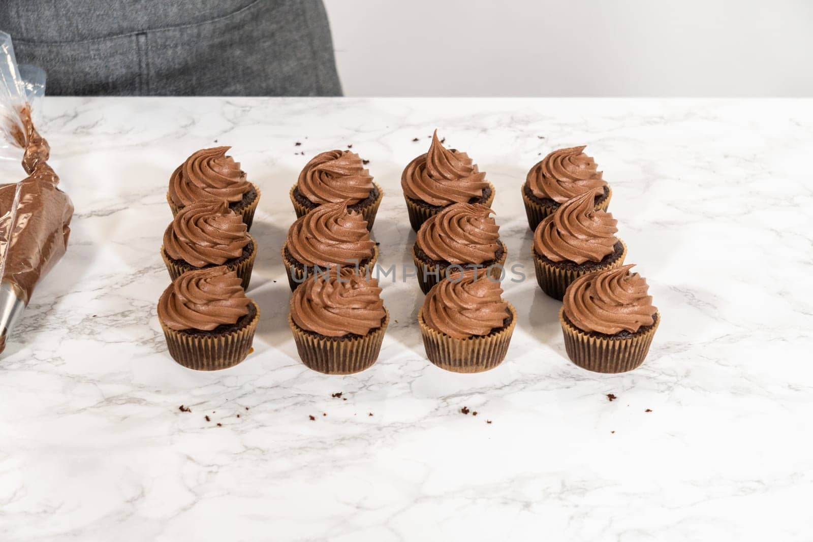 Delicate swirls of rich chocolate icing are meticulously piped onto each chocolate cupcake, creating an irresistible treat.