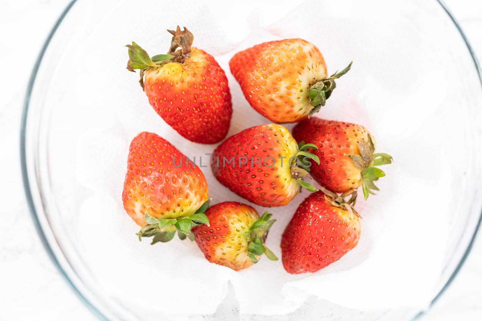 Freshly washed and dried strawberries are carefully arranged in a glass bowl lined with paper towel, ready for snacking or further use.