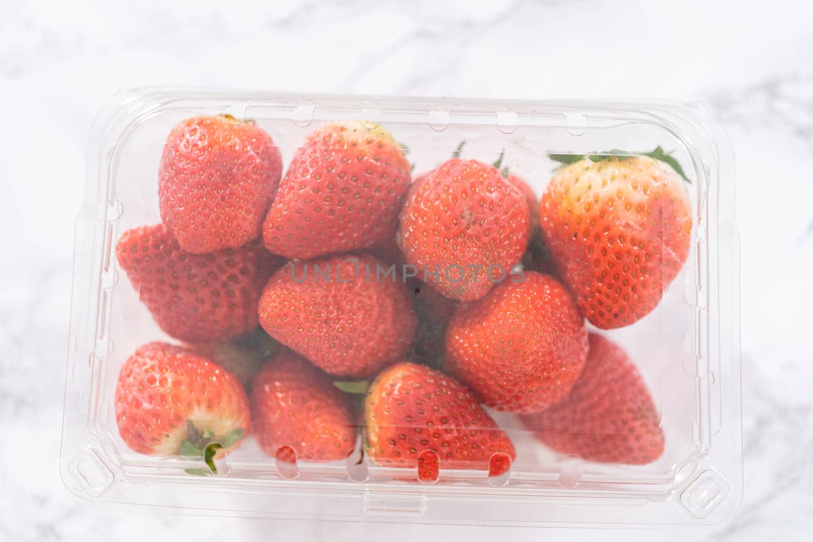 Fresh strawberries are showcased in their original store-bought plastic container, resting on a kitchen counter, ready to be washed, eaten, or stored.