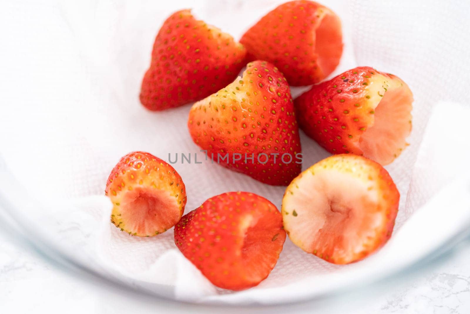 Freshly washed and dried strawberries are carefully arranged in a glass bowl lined with paper towel, ready for snacking or further use.