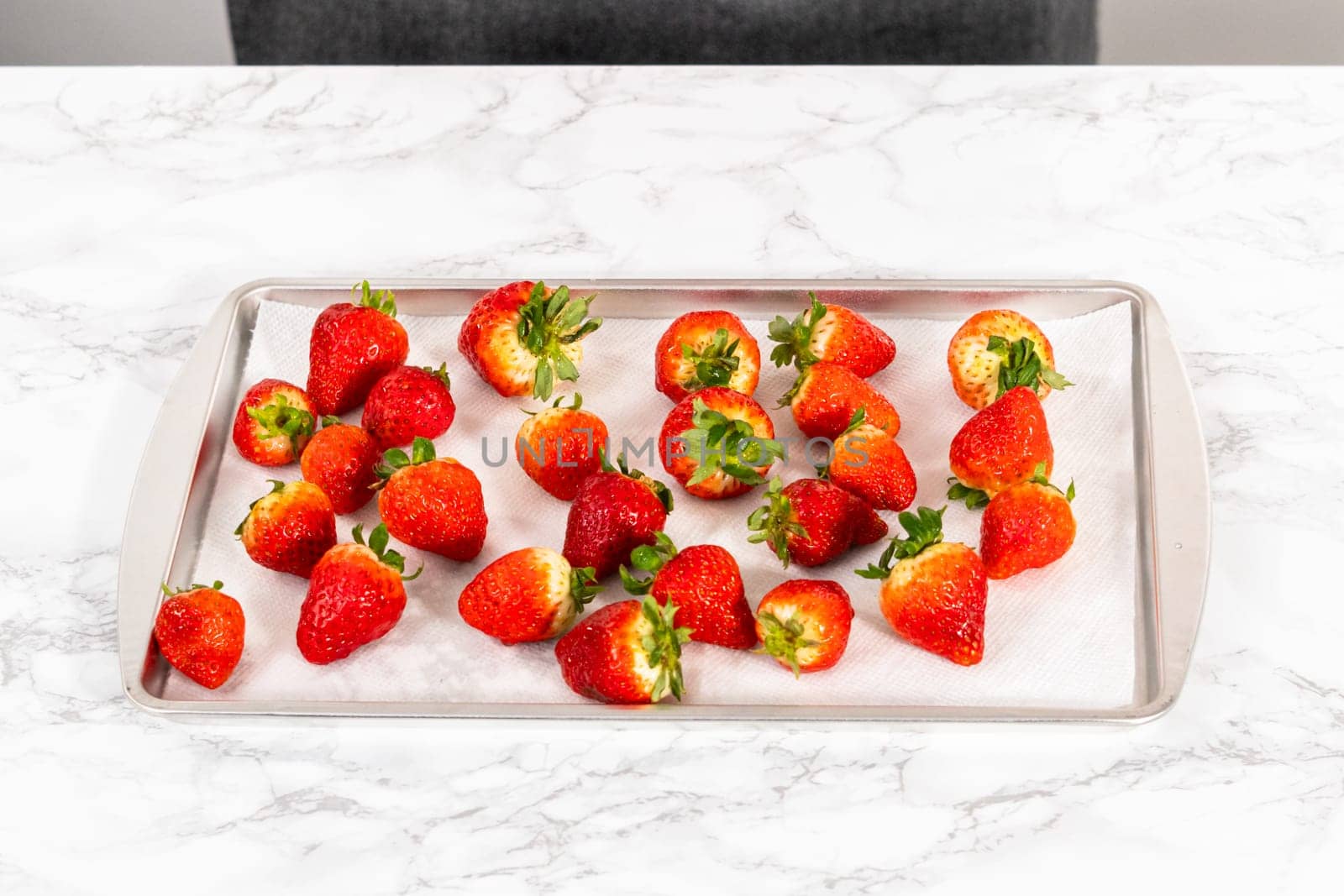 Juicy red strawberries, freshly washed, are spread out to dry on a baking sheet, carefully lined with paper towels to absorb excess moisture and prevent mold.