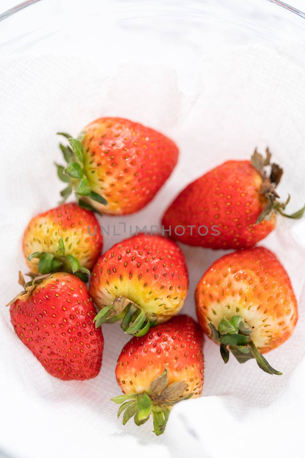 Freshly washed and dried strawberries are carefully arranged in a glass bowl lined with paper towel, ready for snacking or further use.