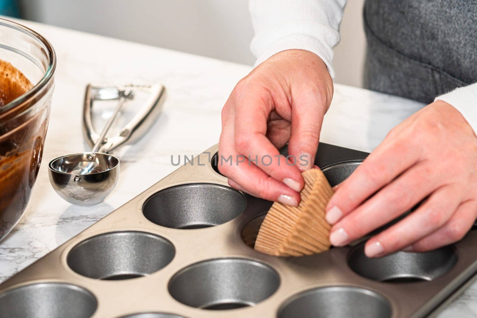 Getting ready to bake delicious chocolate cupcakes, we carefully line the cupcake pan with paper liners, ensuring a delightful treat awaits.