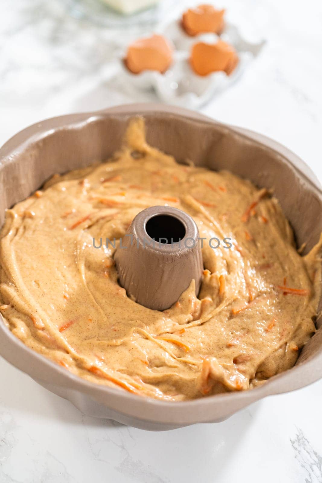 The greased bundt cake pan is filled with cake batter, ready to be baked into a delectable Carrot Bundt Cake.