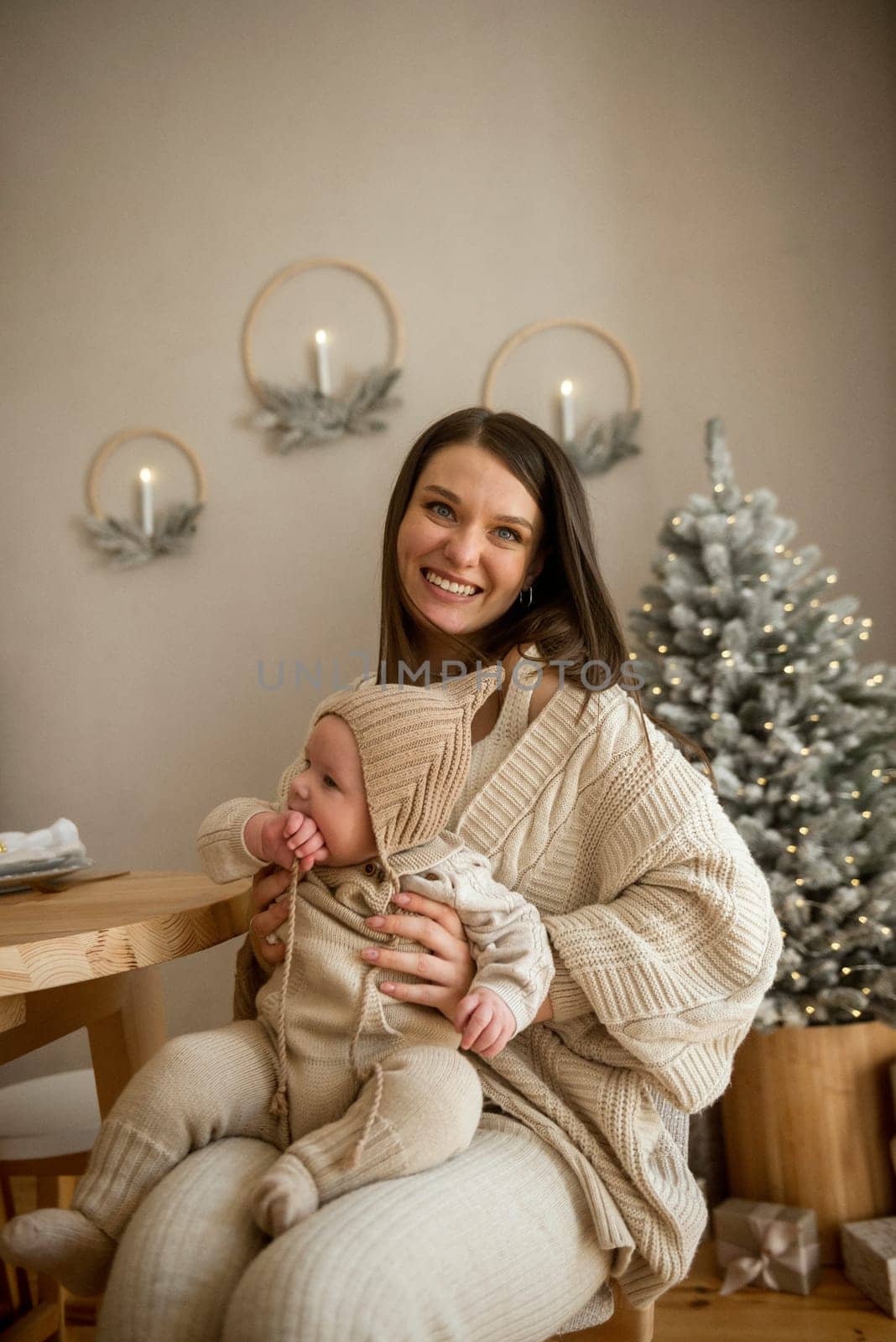 A woman holding a baby.The girl holds her child in her arms. The child is wearing a beige hand-knitted hat. mother and child are happy, they are smiling. They celebrate Christmas.