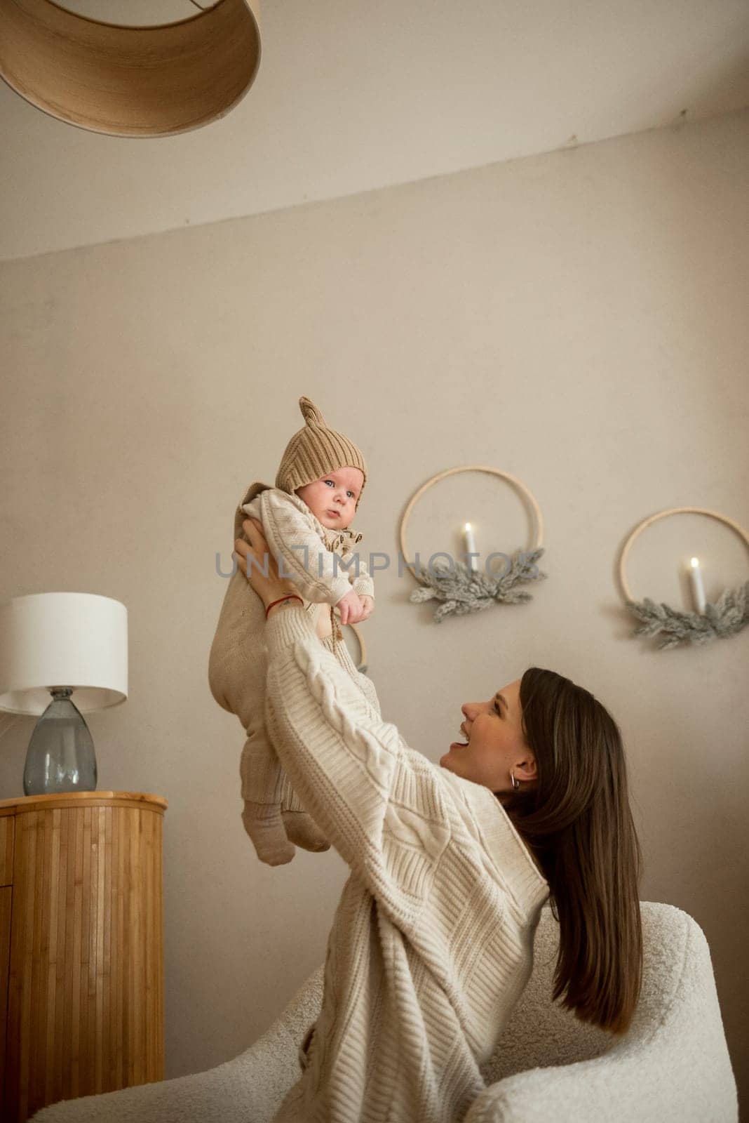 A woman holding a baby. High quality photo, The girl holds her child in her arms. The child is wearing a beige hand-knitted hat. mother and child are happy, they are smiling